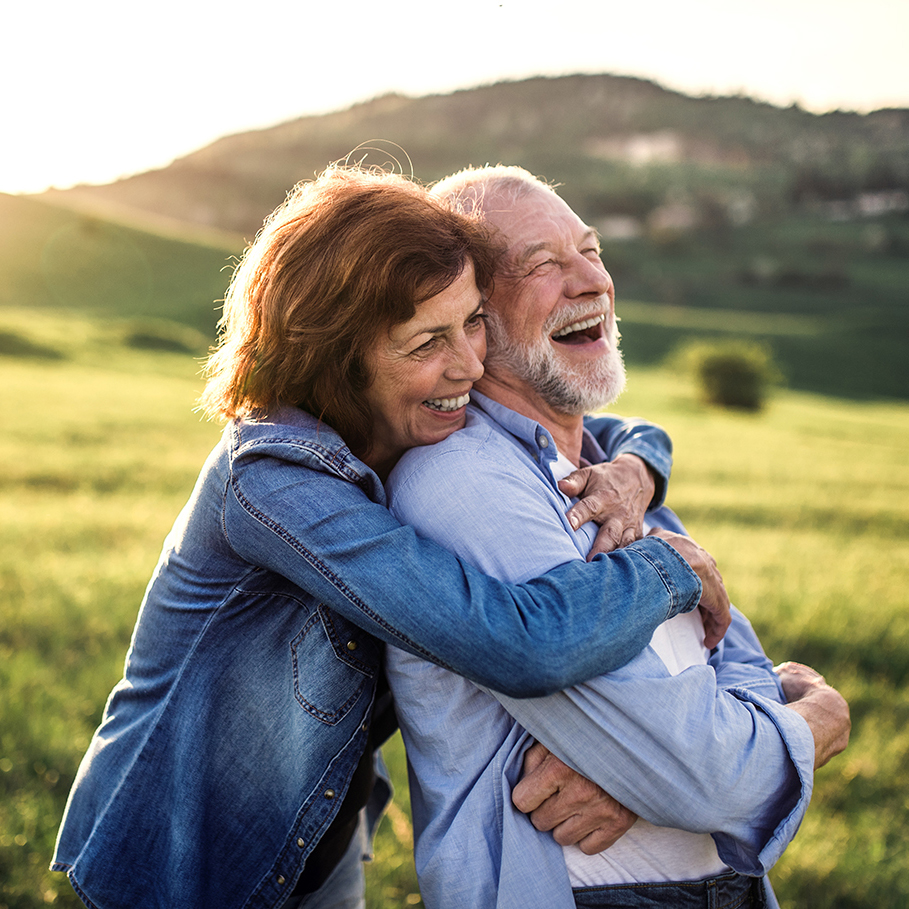 Side view of senior couple hugging outside in spring nature at sunset.
